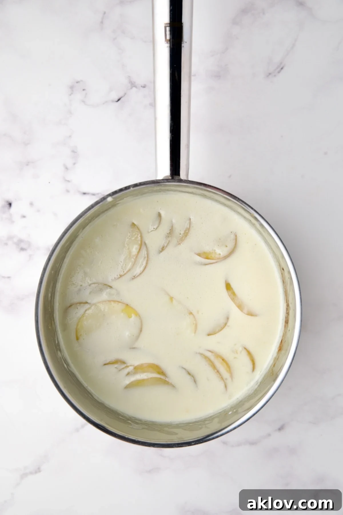 Partially cooked Yukon Gold potatoes simmering in cream within a stainless steel saucepan, visibly softened.