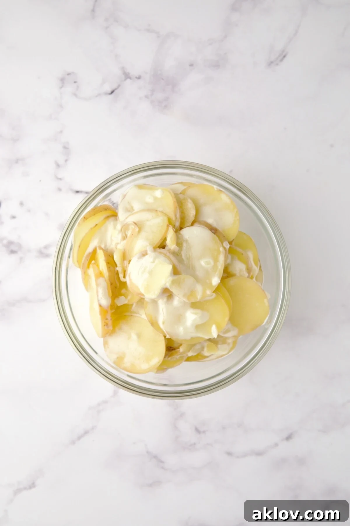 Cooked Yukon Gold potatoes, onion, and garlic transferred to a glass bowl using a slotted spoon.