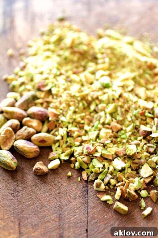 Photo of finely chopped pistachios on a wooden surface, with some whole pistachios scattered around.