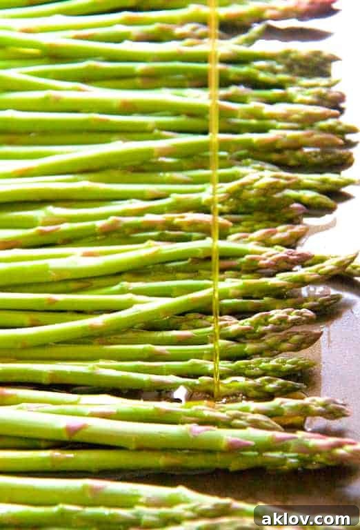 Photo of fresh asparagus spears being drizzled with olive oil on a baking sheet.