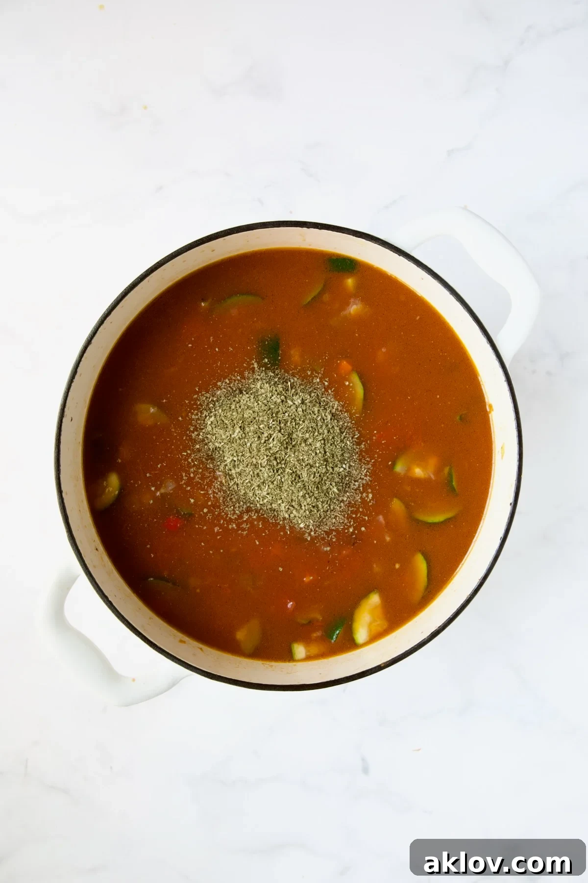 Italian seasoning being added to the simmering soup in a white Dutch oven.