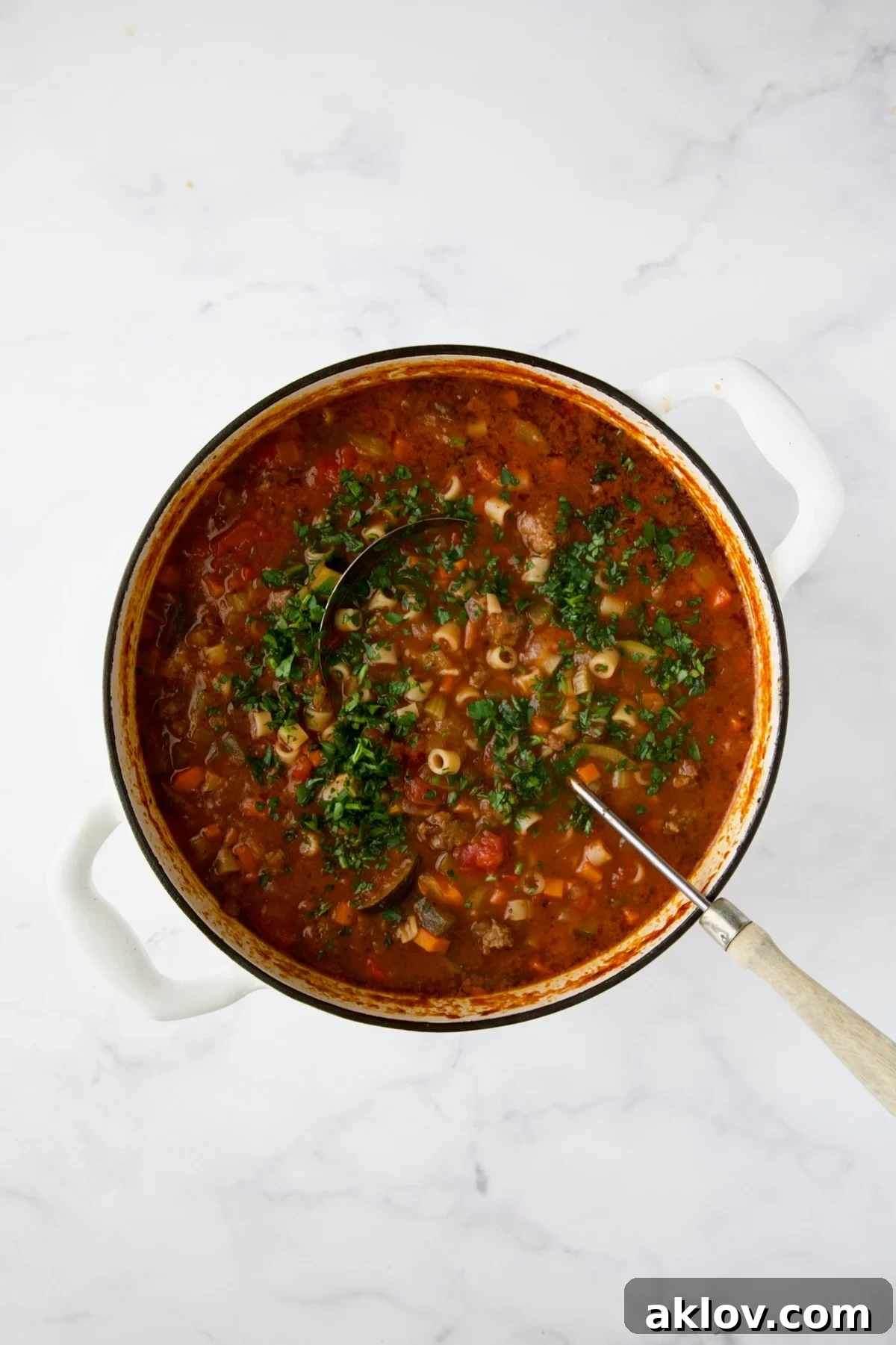 A ladle in a white Dutch oven filled with finished Italian Sausage Soup, garnished with parsley.