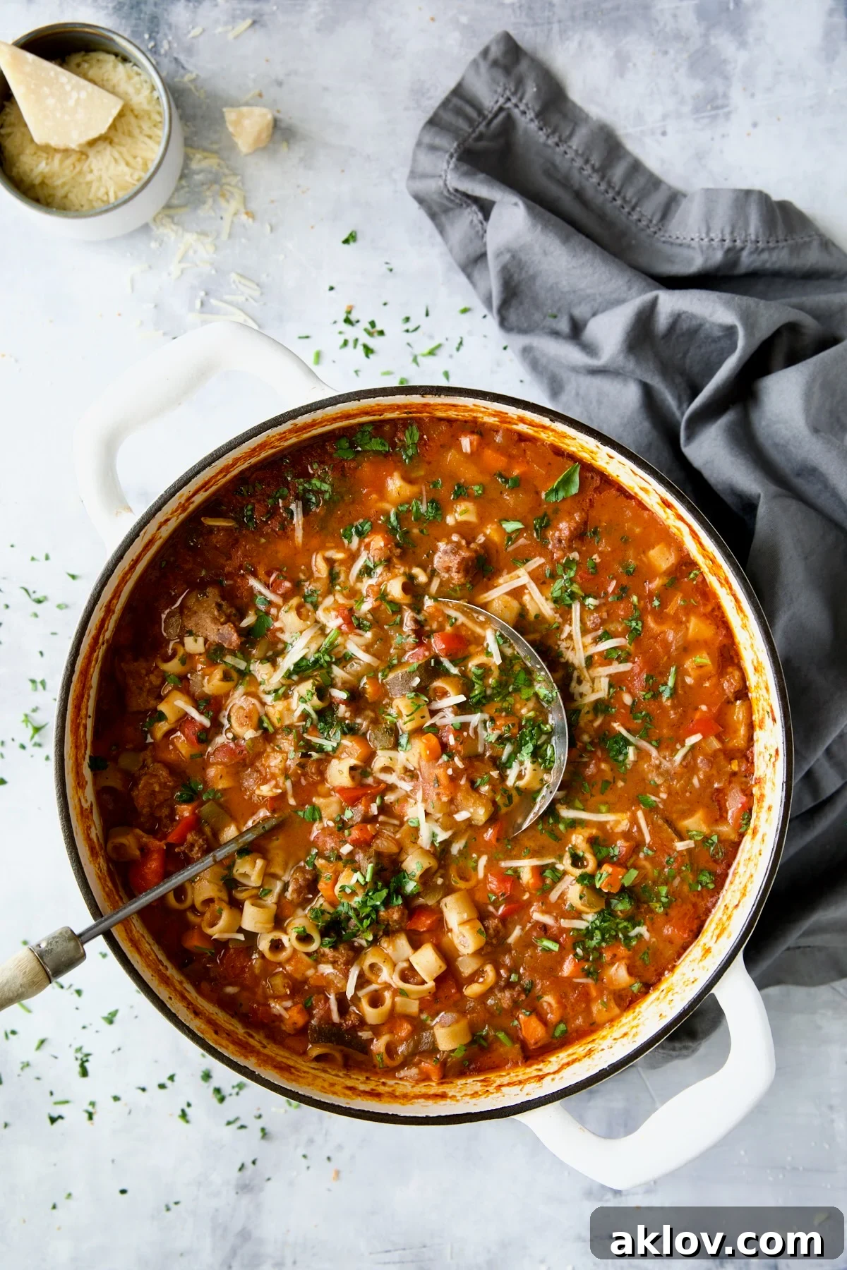 Italian Sausage Soup in white Dutch oven garnished with fresh parsley and Parmesan cheese, close-up.