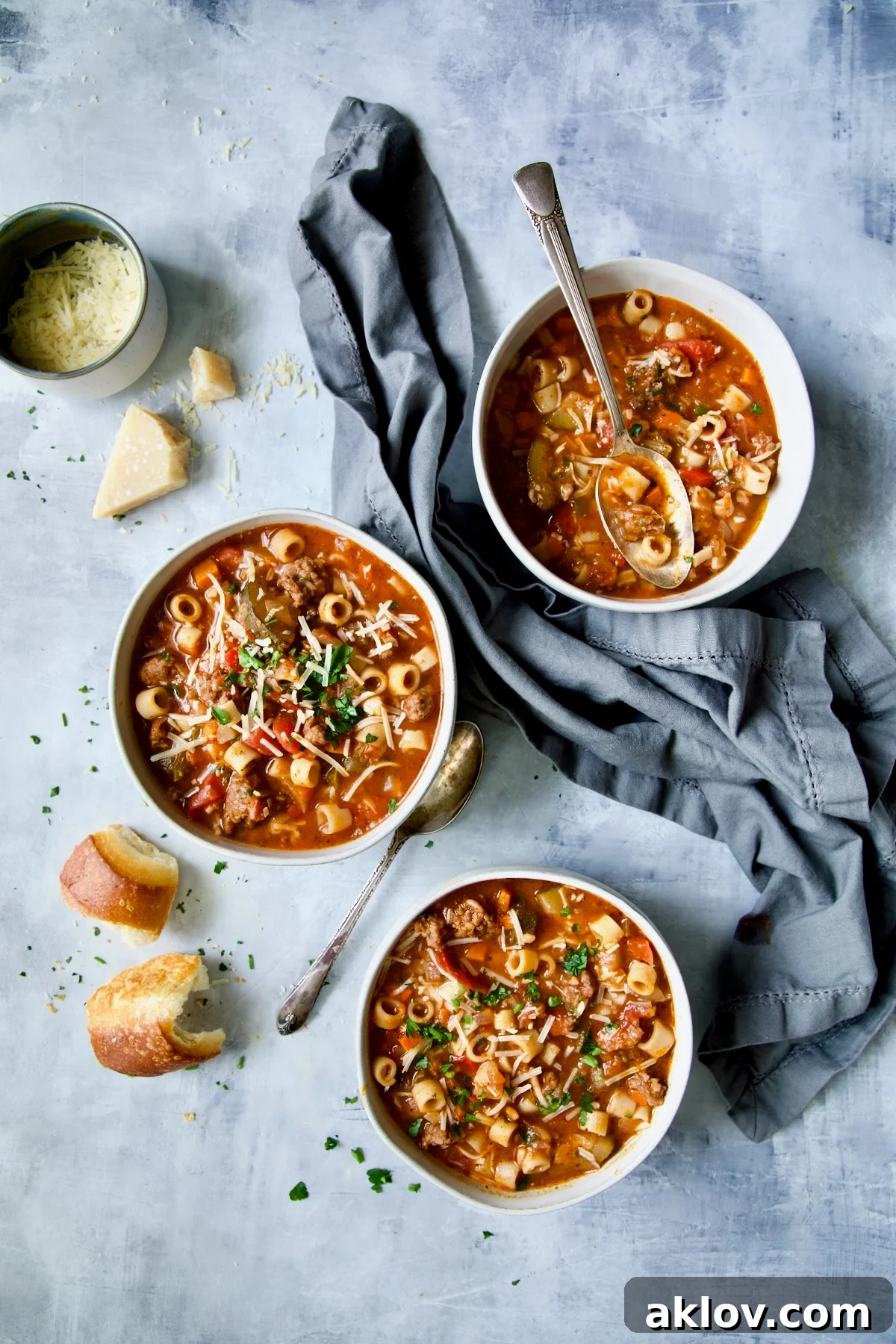 Three bowls of Italian Sausage Soup on a blue background with a blue napkin, ready to be enjoyed.