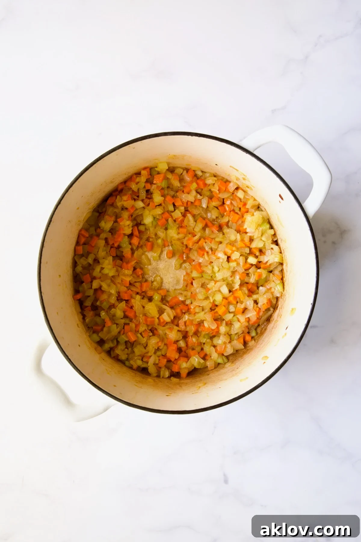 Adding celery and carrots to sautéed onions in a white Dutch oven.