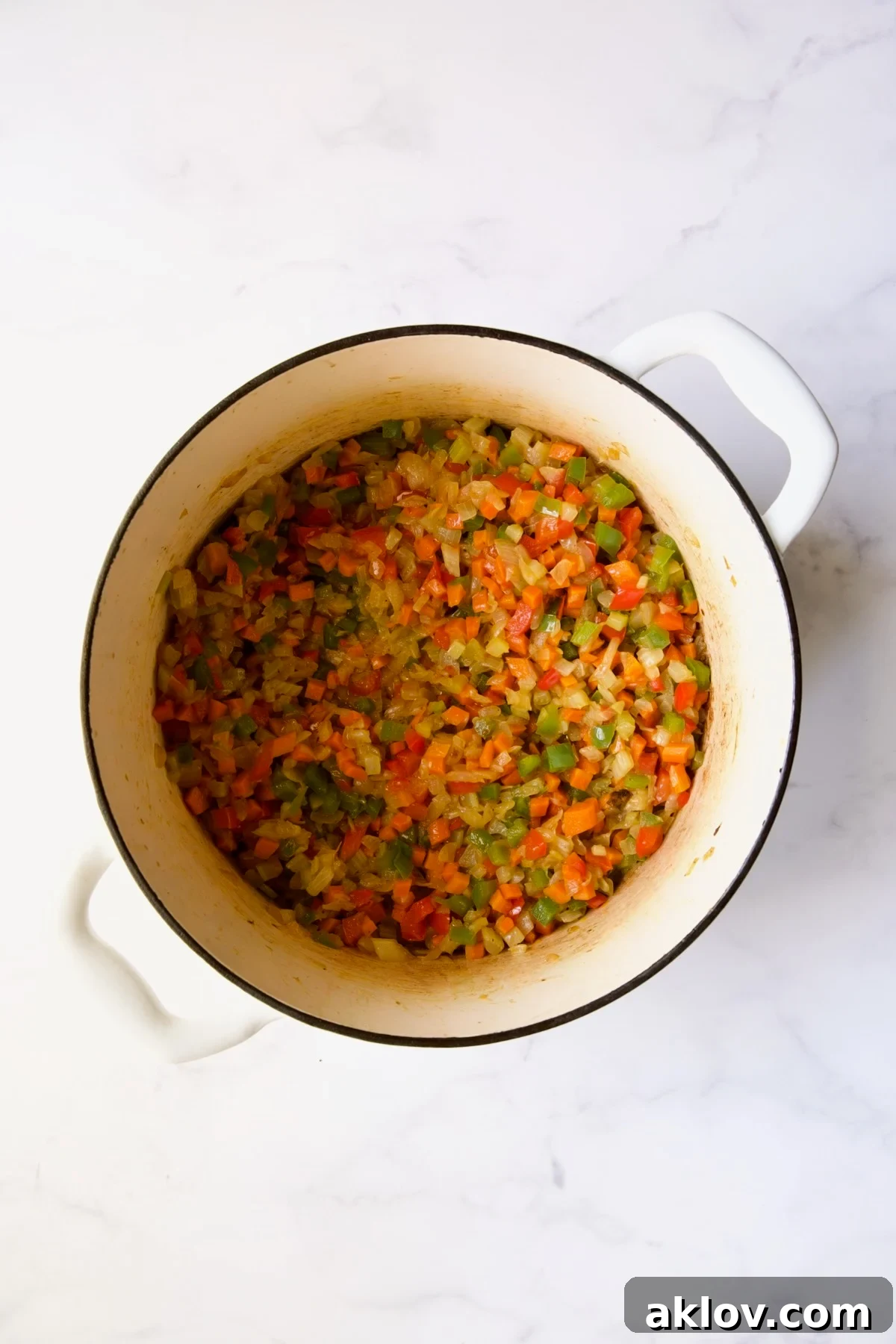 Chopped bell peppers added to the sautéed mirepoix in a white Dutch oven.