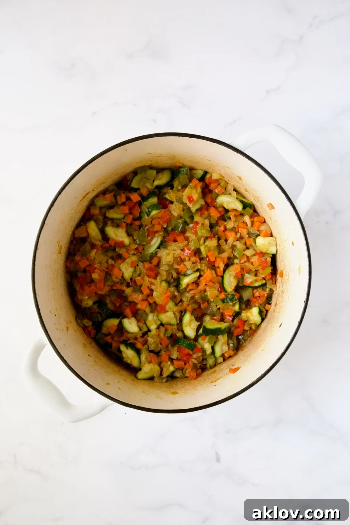 All cooked vegetables for the Italian sausage soup in a white Dutch oven.