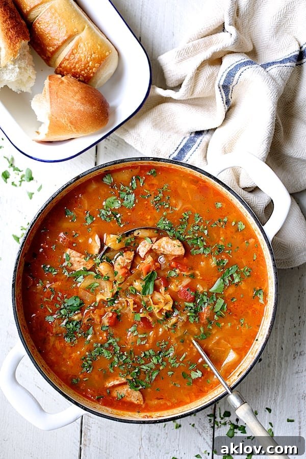 Smoky Kielbasa and Cabbage Stew with White Beans 3 A white Dutch oven filled with Farmhouse Cabbage Soup with Cannellini Beans and Kielbasa, accompanied by a serving of crusty bread on the side.