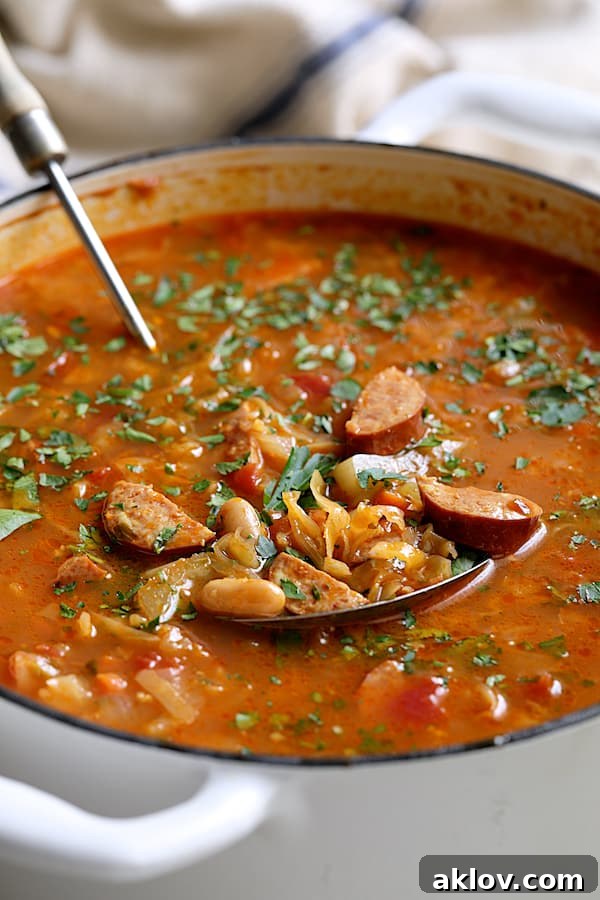 Smoky Kielbasa and Cabbage Stew with White Beans 4 A close-up shot of the rich texture and ingredients of Farmhouse Cabbage Soup with Cannellini Beans and Kielbasa in a white Dutch oven.