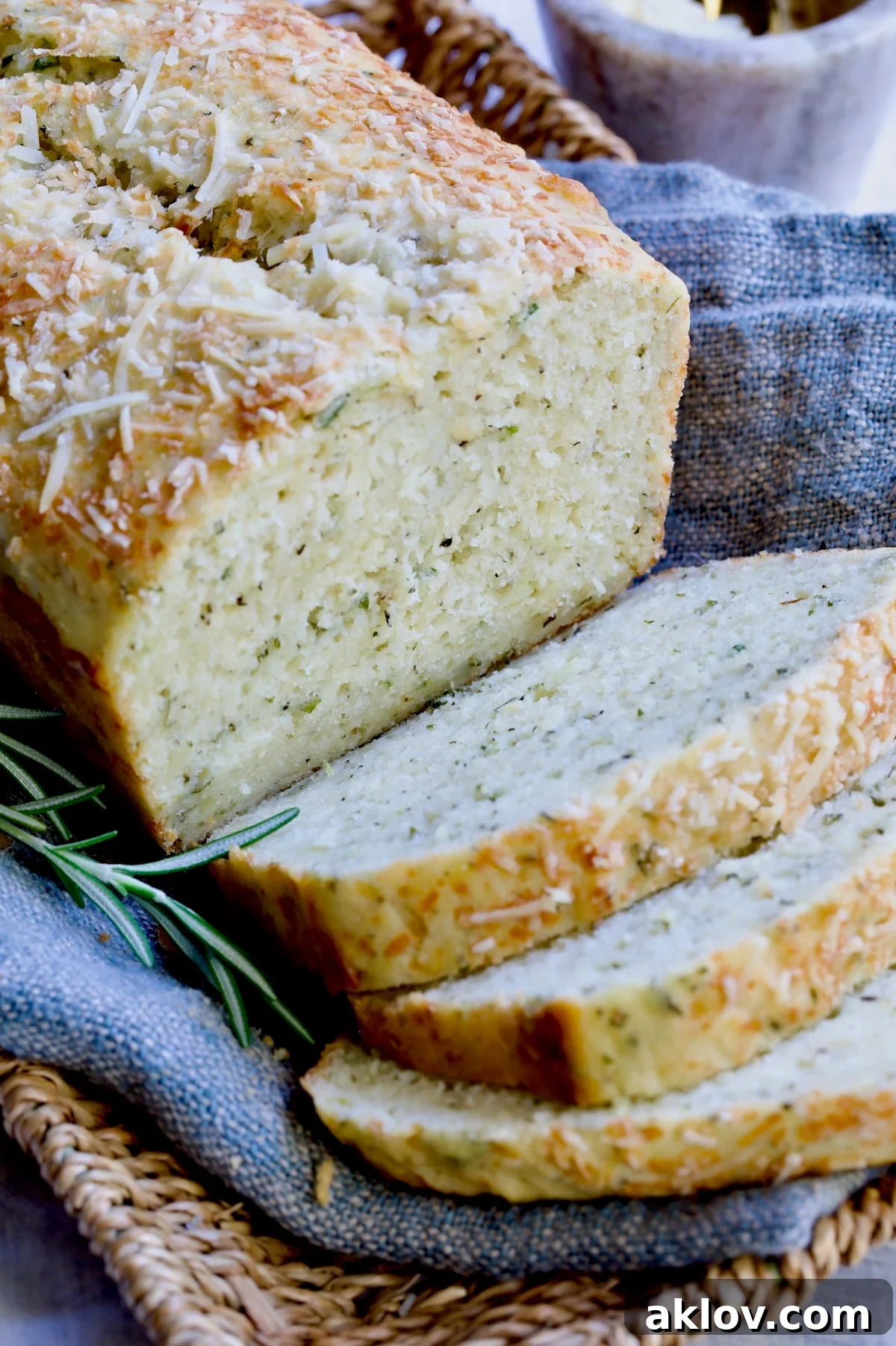 A sliced loaf of Easy Herb Bread displayed on a blue napkin within a wicker basket.