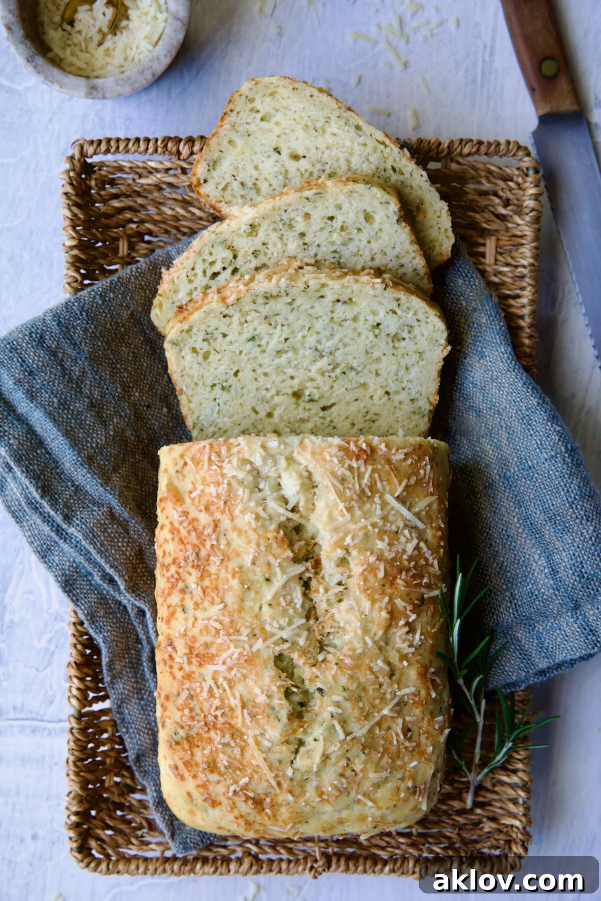 Sliced loaf of Easy Herb Bread on blue napkin in wicker basket.