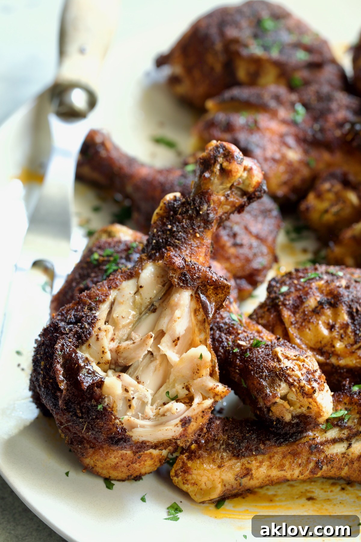 Baked Cajun Chicken Drumsticks on an oval white platter, with one drumstick partly shredded, showcasing its deliciousness.