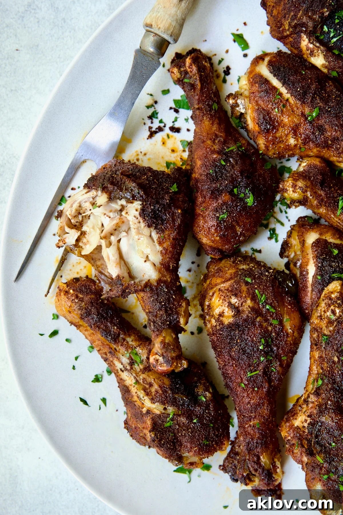 Baked Cajun Chicken Drumsticks on an oval white platter, with one drumstick partly shredded to show its tenderness.