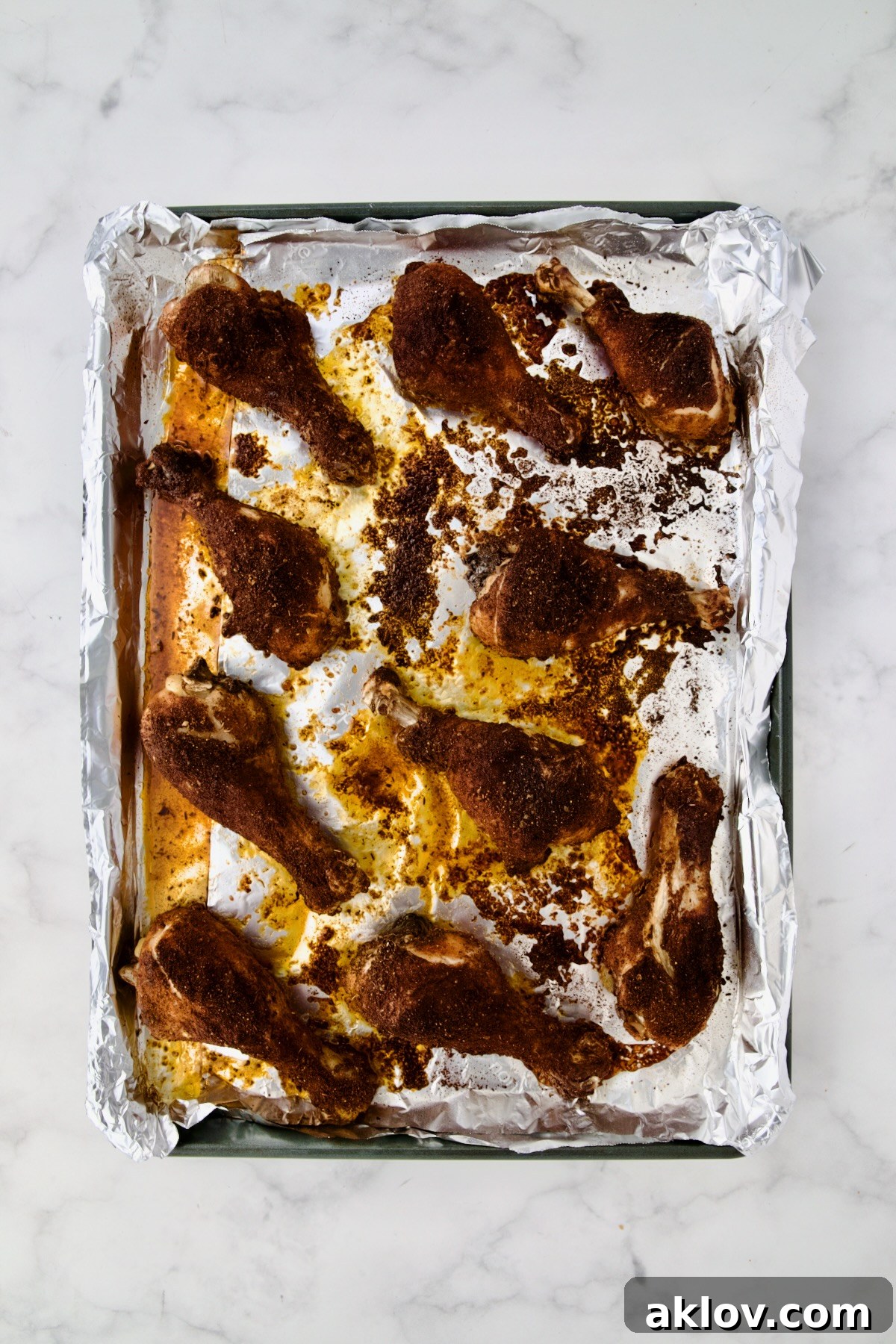 Ten cooked Baked Cajun Chicken Drumsticks cooling on an aluminum foil-lined rimmed sheet pan after baking.