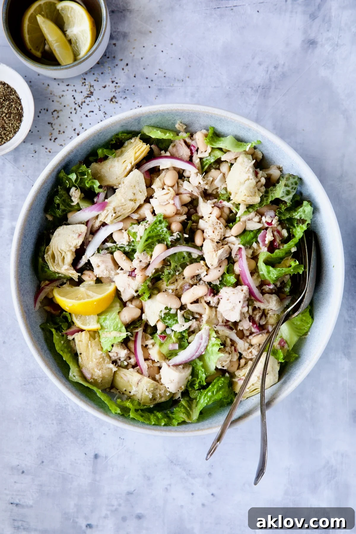 Tuna, White Bean and Artichoke Salad in serving bowl with serving utensils on blue background.