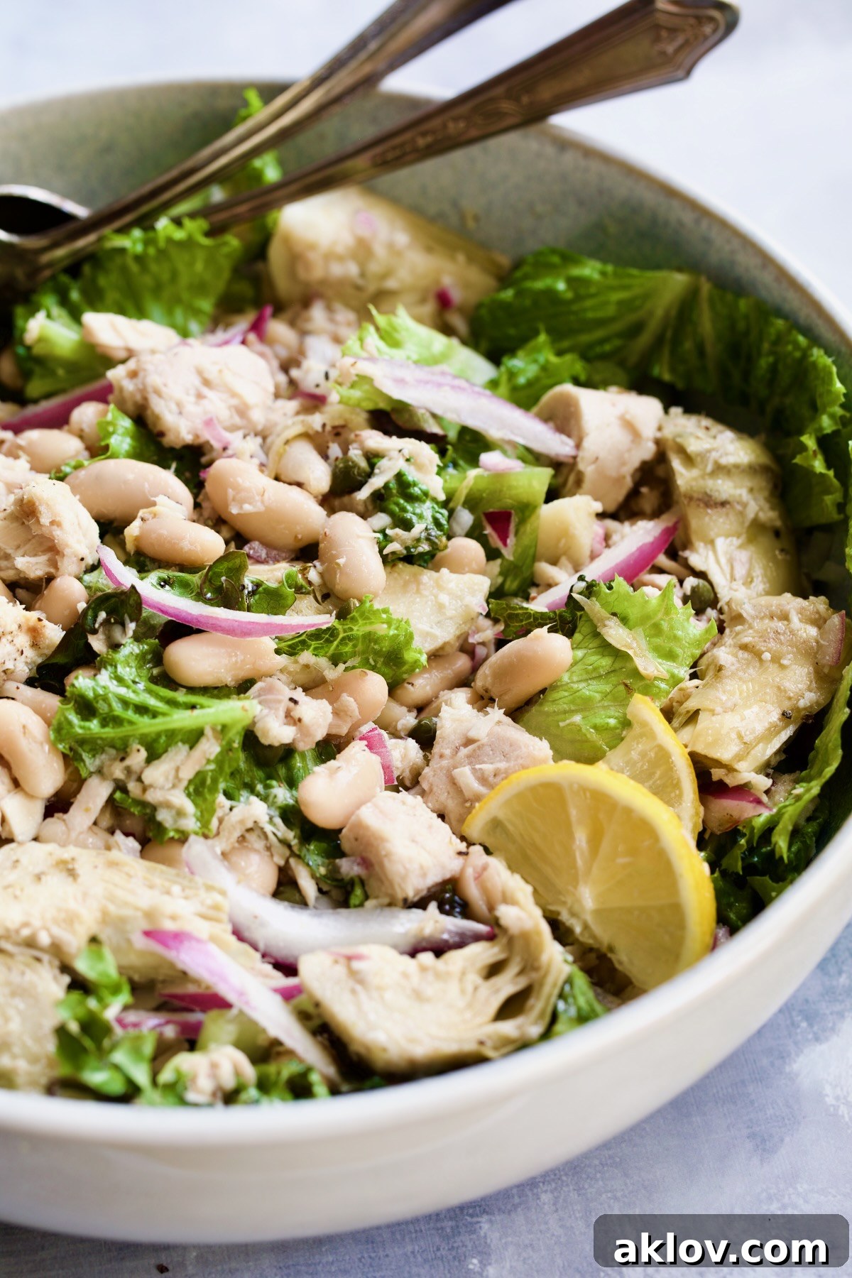 Tuna, White Bean and Artichoke Salad in white serving bowl with silver serving utensils.