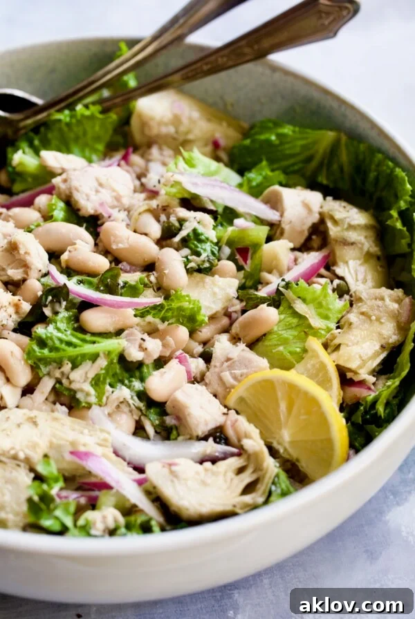 Finished salad in white serving bowl with silver serving utensils.