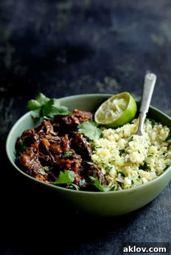 Slow Cooker Beef Short Ribs Barbacoa with Cilantro Lime Cauliflower Rice - Close-up in green serving bowl garnished with cilantro and lime