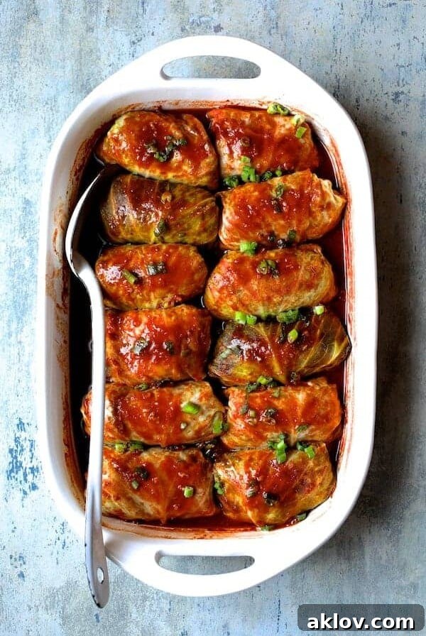 Spicy Asian Pork Cabbage Rolls in white baking dish with white serving spoon after being baked.