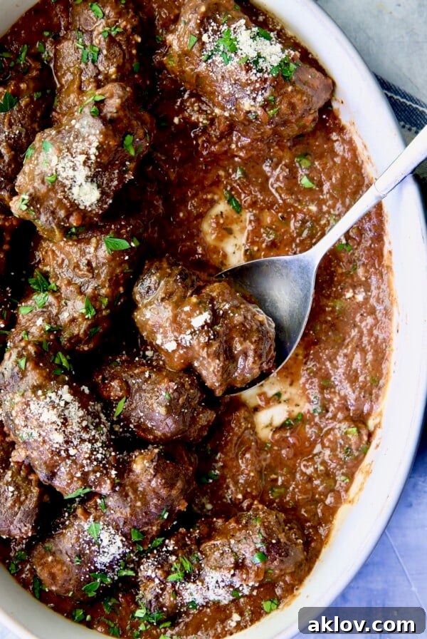 Beef Braciole in oval white serving dish with serving spoon.