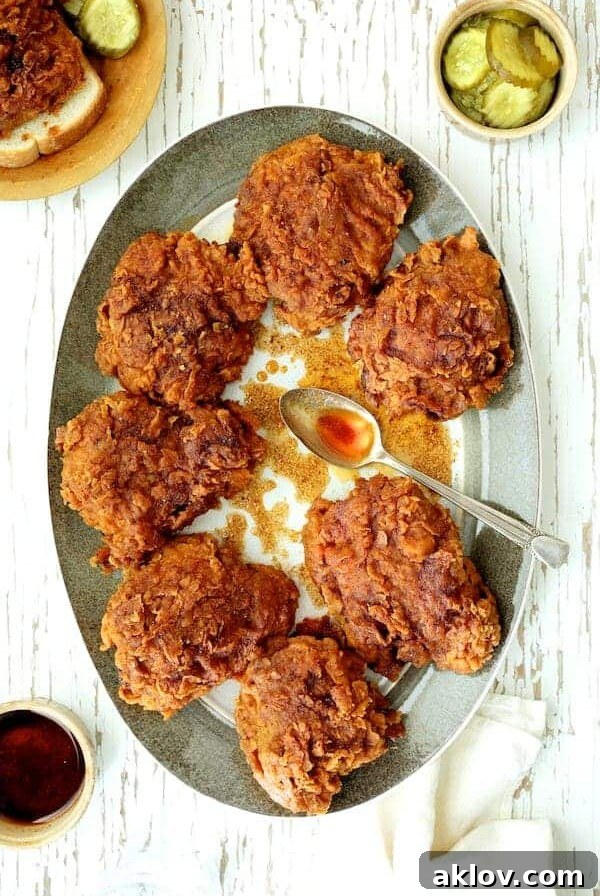 Nashville Style Hot Fried Chicken Hero Shot - Chicken on gray rimmed plate drizzled with hot sauce. Crispy, golden-fried chicken coated in a fiery, iconic Nashville hot sauce, served with pickles.
