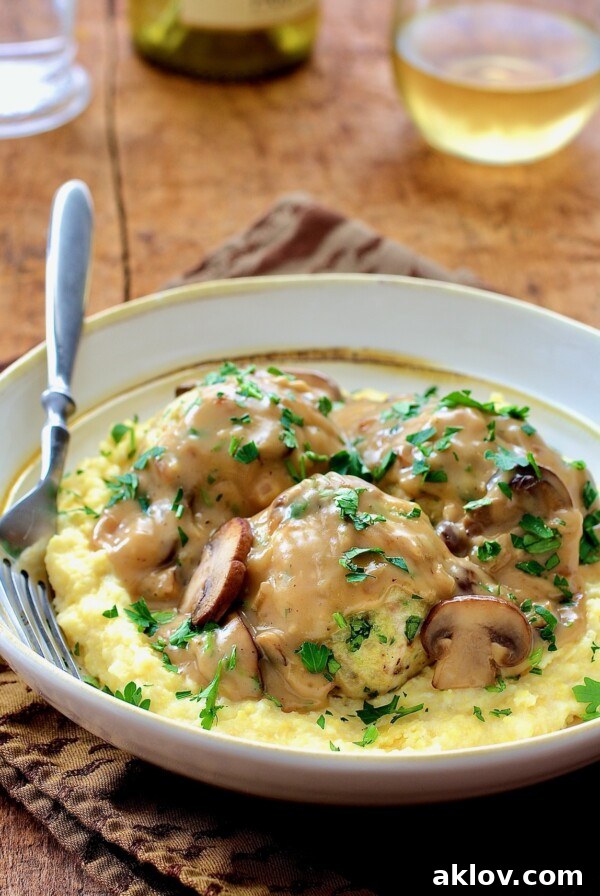 Chicken Meatballs Marsala with Parmesan Polenta in white bowl with fork. Succulent chicken meatballs simmered in a rich Marsala wine sauce, served alongside creamy Parmesan polenta for a comforting Italian meal.