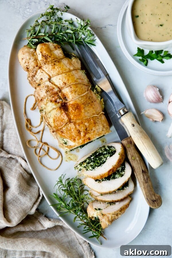 Spinach and Ricotta Stuffed Turkey Breast with Garlic - Herb Sauce on white oval platter garnished with fresh herbs.