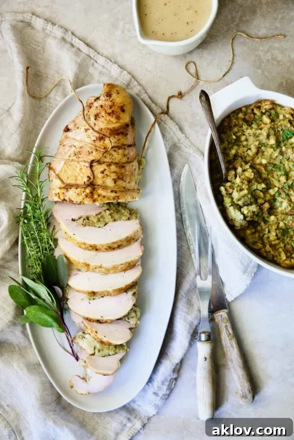 Roast Turkey Breast with Traditional Stuffing on white platter garnished with fresh herbs.