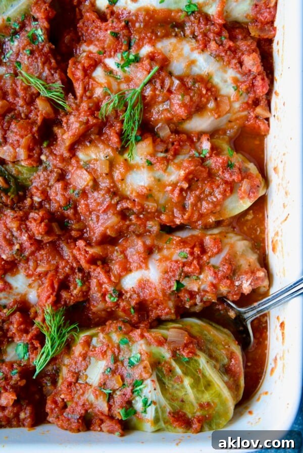 Row of four Polish Stuffed Cabbage in white baking dish with serving fork garnished with fresh dill.