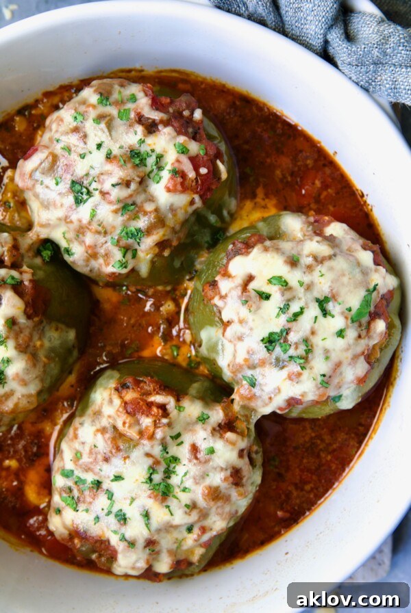 Three Italian Stuffed Peppers in deep white round baking dish. Bell peppers filled with a savory mixture of meat, rice, and cheese, baked until tender in a flavorful tomato sauce.