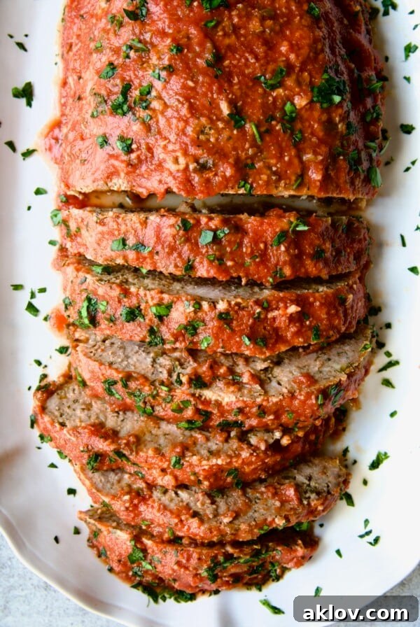 Italian Meatloaf on white platter with half of it sliced. A classic meatloaf infused with Italian herbs and cheeses, baked to perfection and often topped with a tangy tomato glaze.