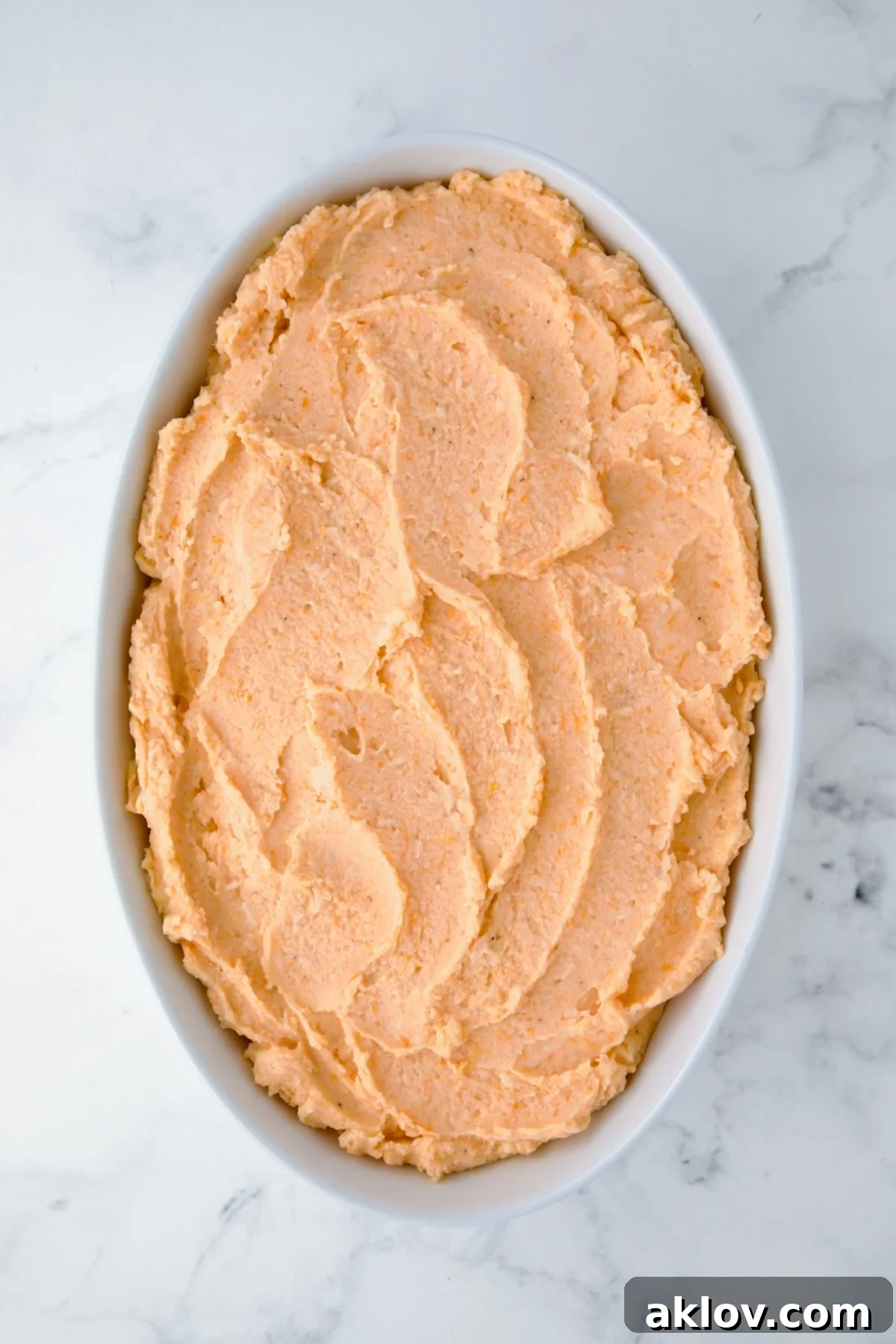Potato and Sweet Potato Bake in white oval baking dish before topping is added and before being baked.