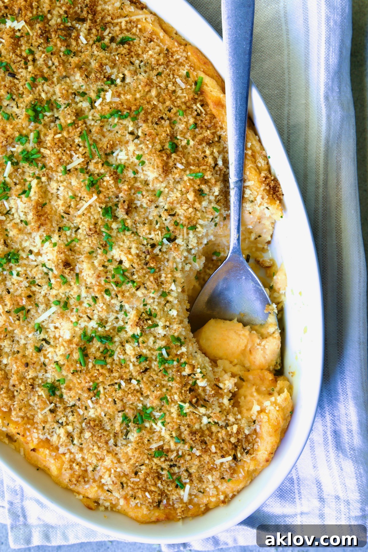 Potato and Sweet Potato Bake in white oval baking dish with silver spoon scooping some out.