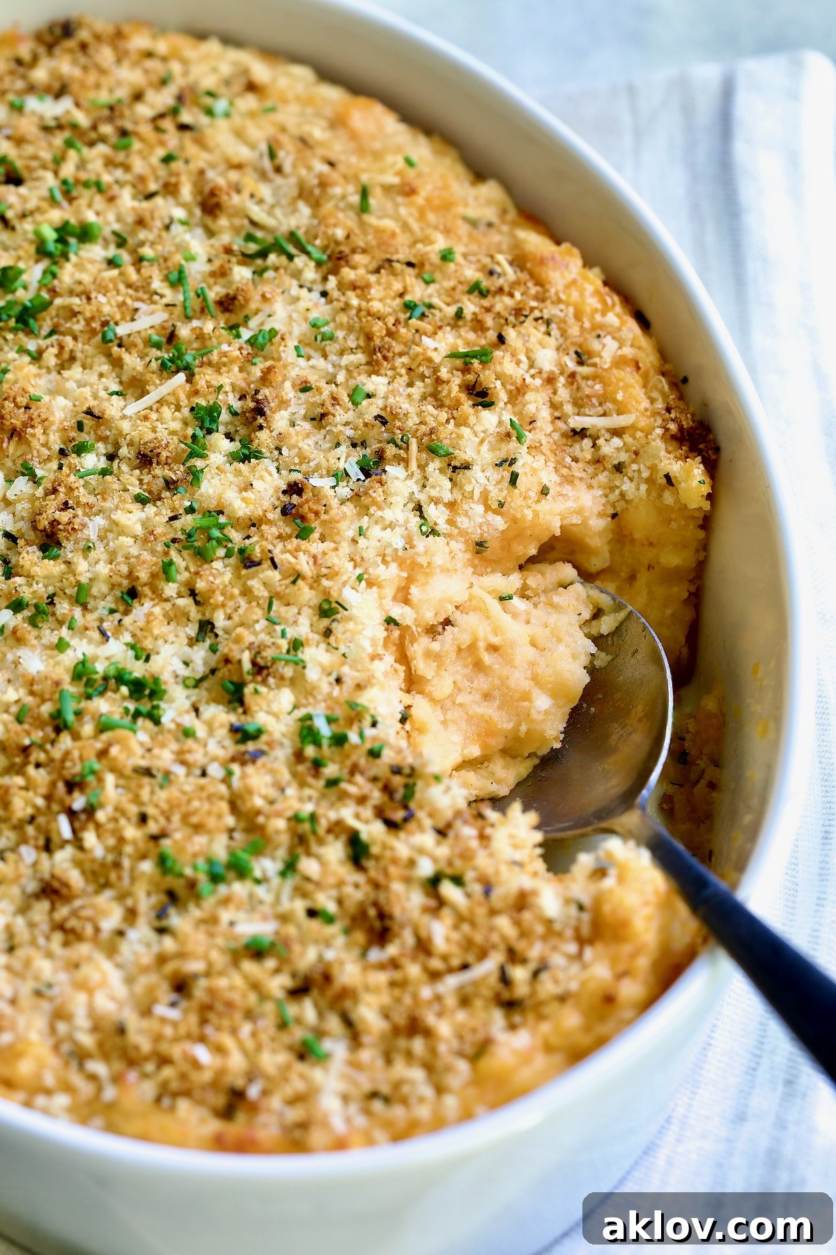 Potato and Sweet Potato Bake in white oval baking dish with silver spoon scooping some out.