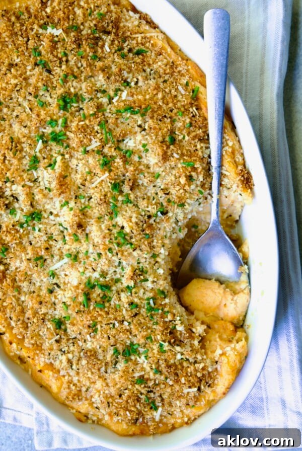 Potato and Sweet Potato Bake in white oval baking dish with silver spoon scooping some out.