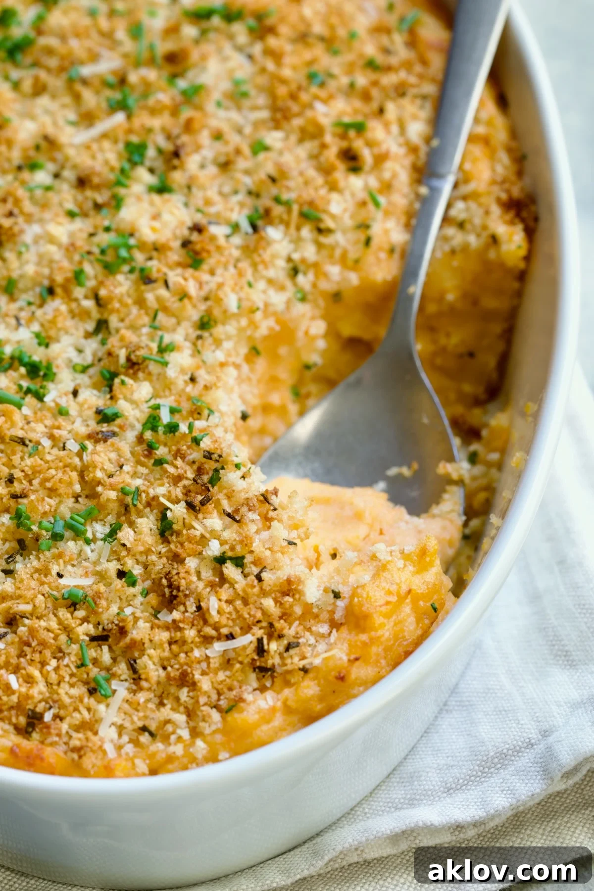Potato and Sweet Potato Bake in white oval baking dish with silver spoon scooping some out.