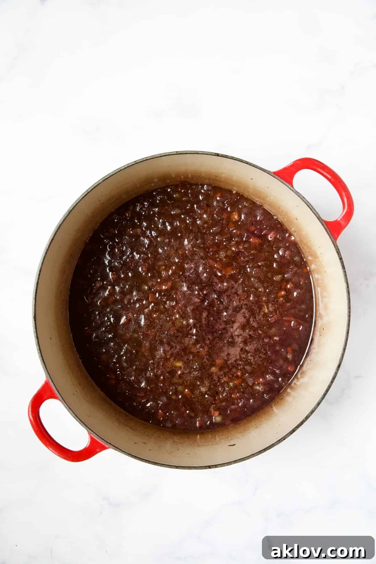 Red wine being added to the cooked vegetables and garlic in a red enamel Dutch oven, initiating the deglazing process.