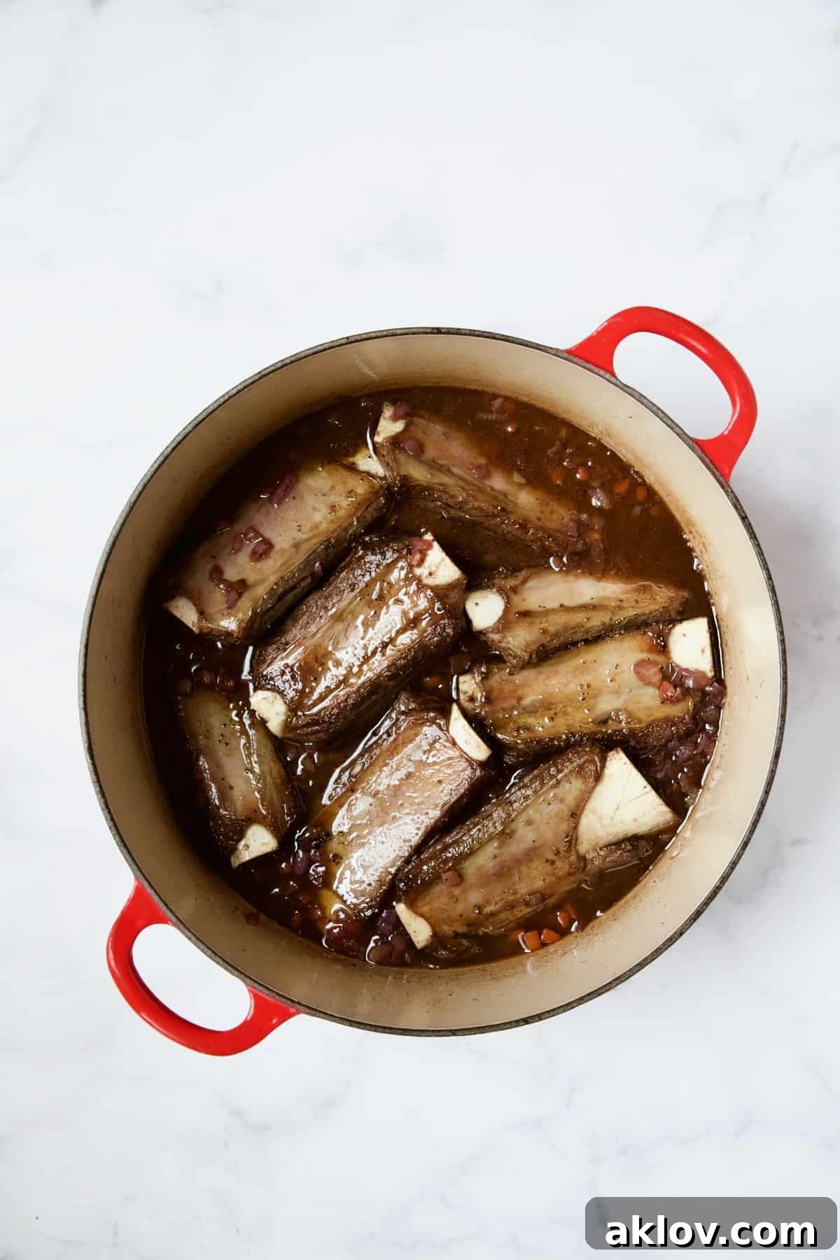 Seared beef short ribs, now placed back into the red wine and vegetable mixture in the red enamel Dutch oven.