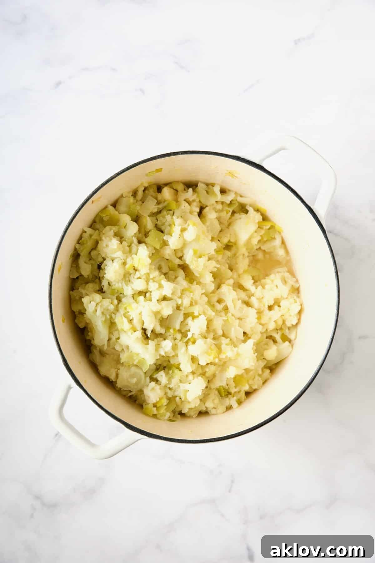 Cooked cauliflower, leeks, garlic, and chicken broth in a white enamel Dutch oven.