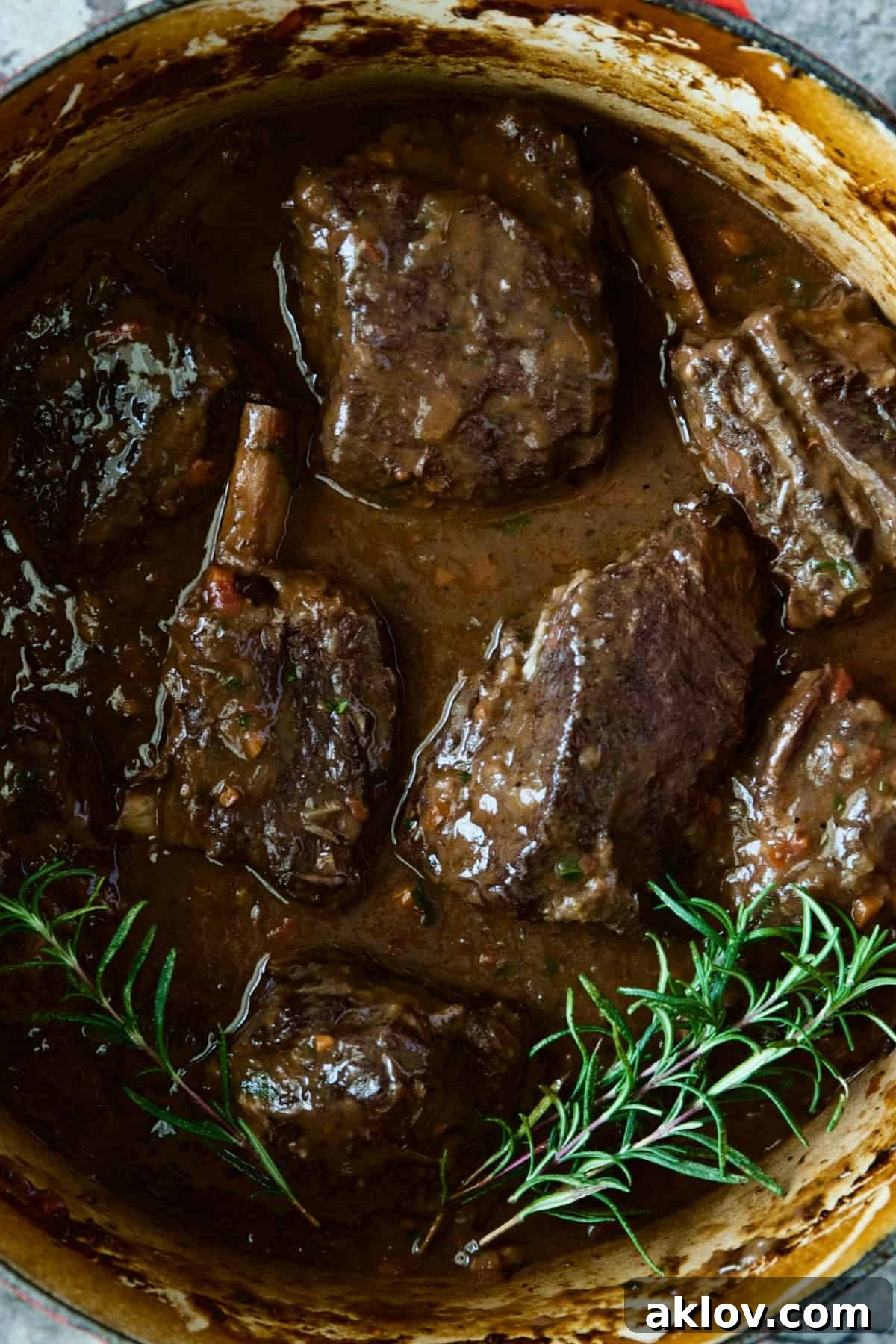 Luxurious Braised Beef Short Ribs in a red Dutch oven, garnished with fresh rosemary sprigs, ready to serve.
