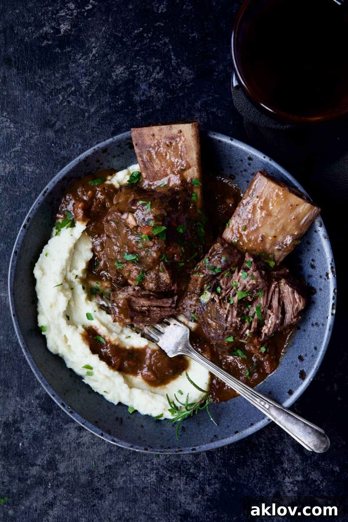 One bowl of Braised Beef Short Ribs with Cauliflower Leek Puree, perfectly presented alongside a wine glass.