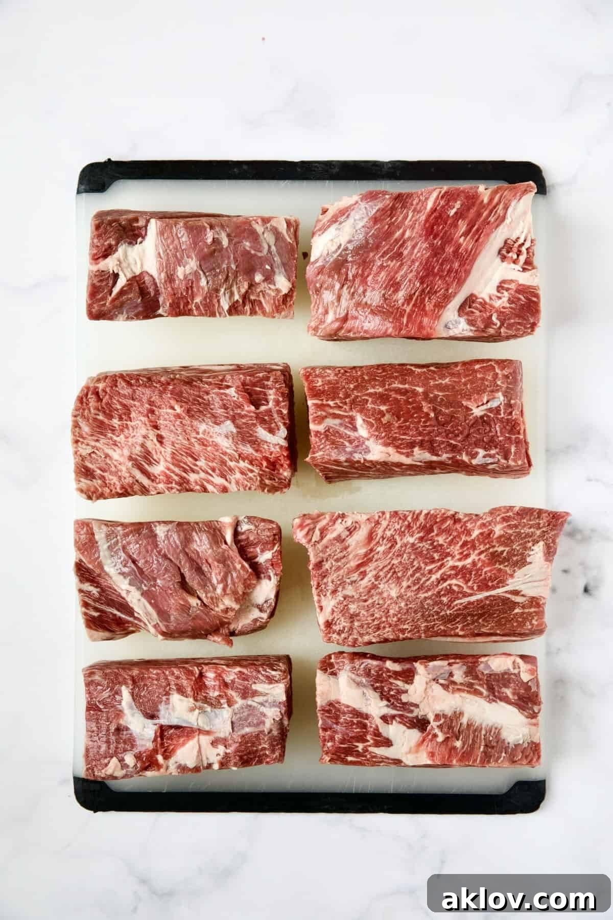 Eight short ribs meticulously arranged on a white plastic cutting board.