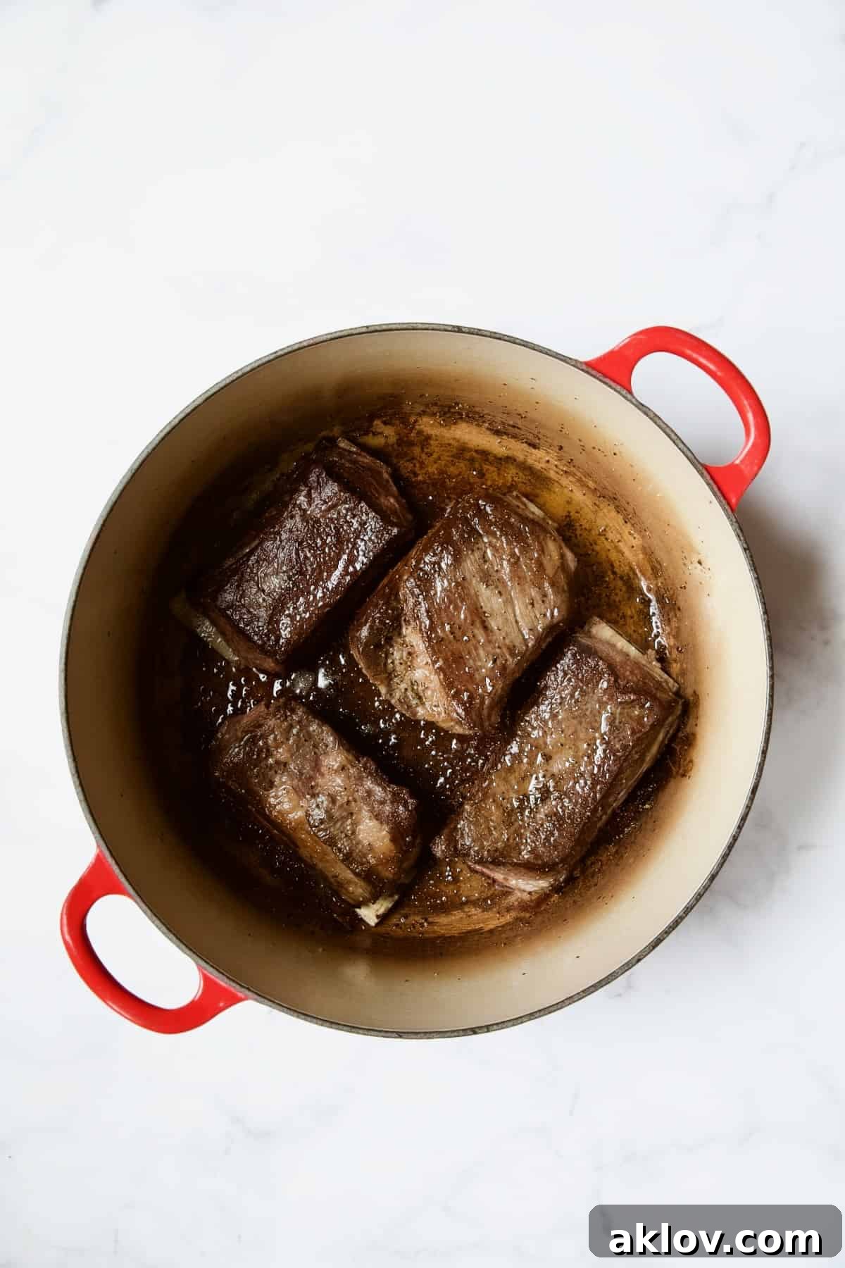 Four beef short ribs beautifully browned in a vibrant red enamel Dutch oven.
