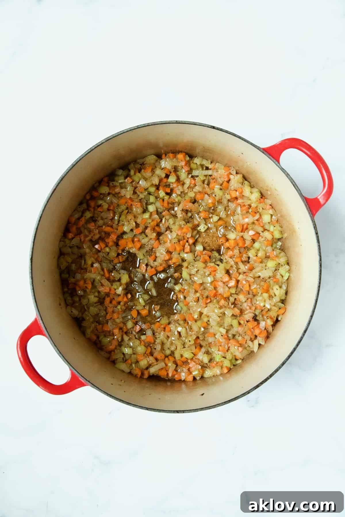 Softened onions, celery, and carrots gently cooking in a red enamel Dutch oven, forming the aromatic base.