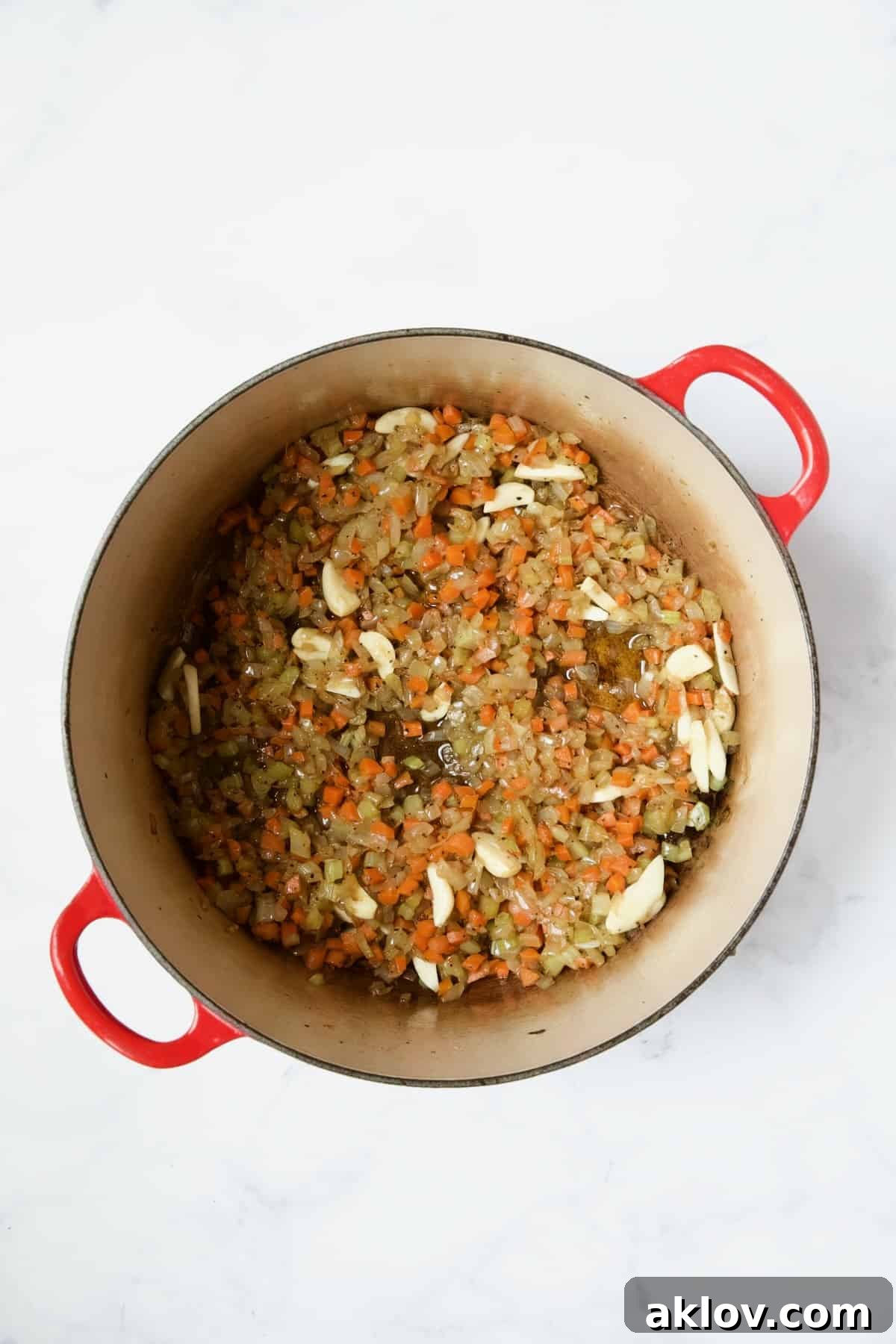 Cooked onions, celery, carrots, and fragrant garlic in a red enamel Dutch oven.