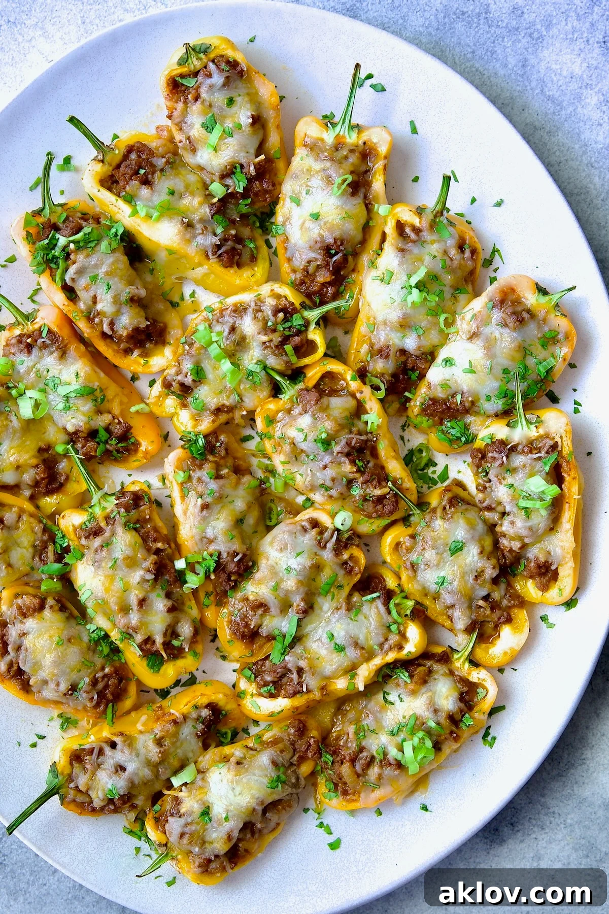 Mini Pepper Taco Poppers 2 Taco-Stuffed Mini Peppers on white oval platter garnished with thinly sliced scallion and chopped cilantro.