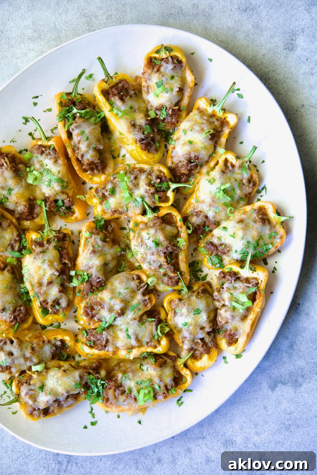 Mini Pepper Taco Poppers 11 Taco-Stuffed Mini Peppers on white oval platter garnished with thinly sliced scallion and chopped cilantro.