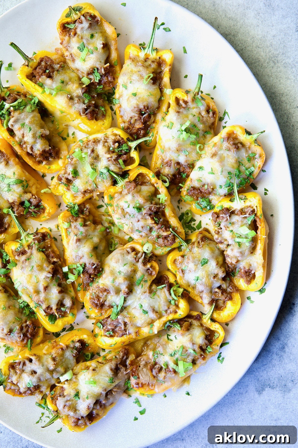 Mini Pepper Taco Poppers 13 Taco-Stuffed Mini Peppers on white oval platter garnished with thinly sliced scallion and chopped cilantro.