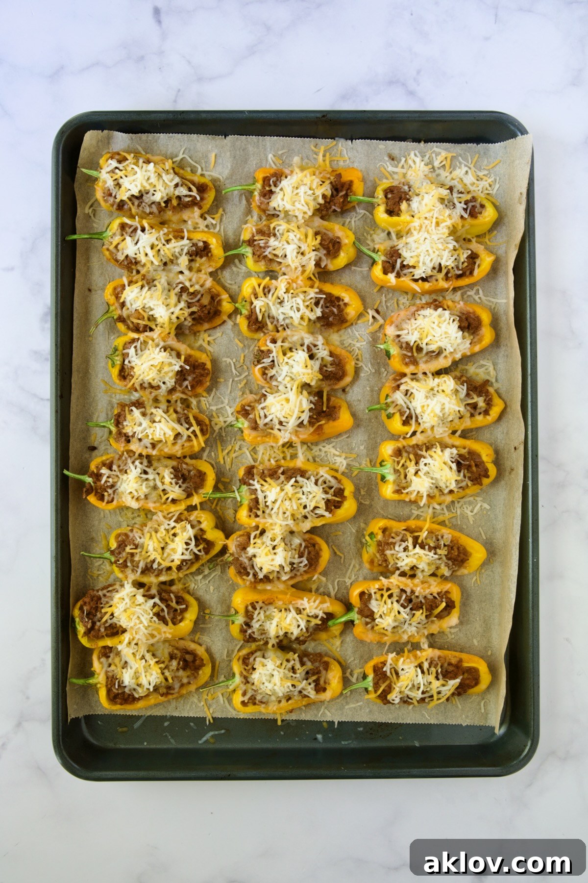 Mini Pepper Taco Poppers 10 Halved, partially baked yellow mini peppers on parchment paper lined baking sheet with shredded Mexican cheese blend added.