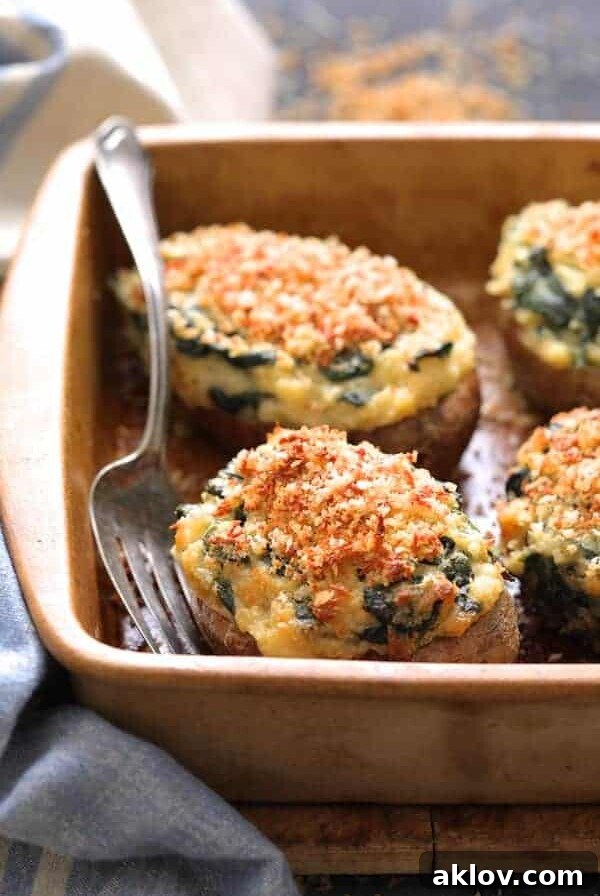 Spinach Parmesan Ranch Twice Baked Potatoes close up shot in clay baking dish with serving fork and blue striped towel, a gourmet twist.